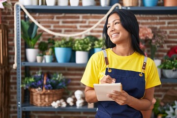 Young beautiful latin woman florist smiling confident writing on notebook at florist