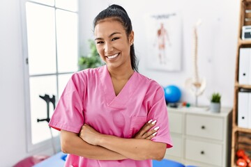 Young hispanic woman working at pain recovery clinic happy face smiling with crossed arms looking at the camera. positive person.