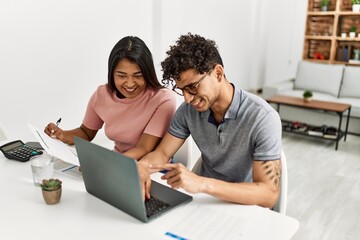 Obraz premium Young latin couple working using laptop sitting on the table at home.