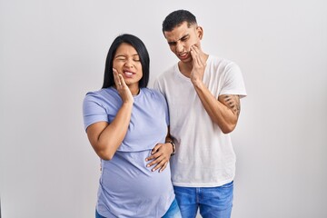 Young hispanic couple expecting a baby standing over background touching mouth with hand with painful expression because of toothache or dental illness on teeth. dentist concept.