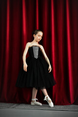 A cute ballerina girl in a black dress on a red background. Art. Dance. Beauty.