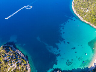 Fototapeta na wymiar aerial view of a paradisiacal Mediterranean bay with turquoise water surrounded by massive mountains, with floating motorboats, with a small bushy island; the bay on the peljesac peninsula seen from a