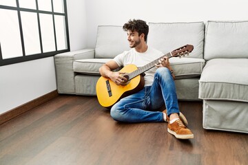 Young hispanic man smiling confident playing classical guitar at home
