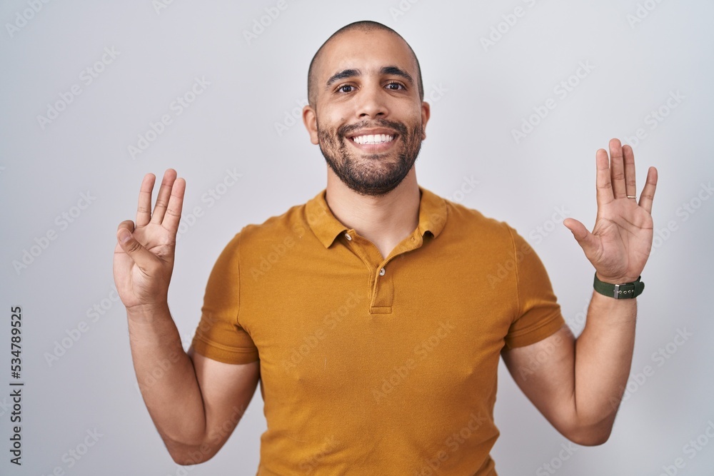 Poster Hispanic man with beard standing over white background showing and pointing up with fingers number eight while smiling confident and happy.