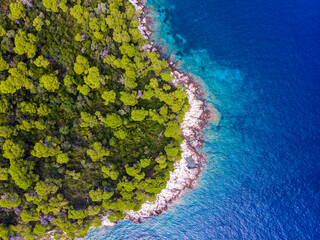 aerial view of a paradisiacal Mediterranean bay with rocky beach, turquoise water and green trees; beautiful beaches of the peljesac peninsula as seen from a drone