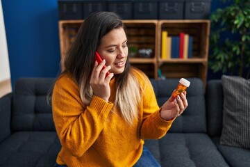 Young beautiful plus size woman talking on smartphone holding pills at home