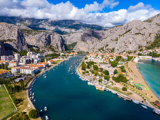 aerial view of the town of omiš in croatia, a picturesque town on the adriatic coast with the mouth of the cetina river, a beautiful beach and mighty mountains in the background as seen from a drone