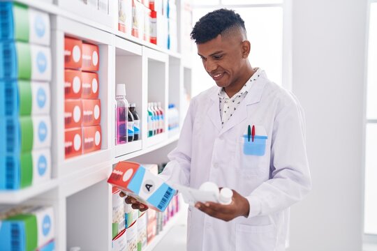 Young Latin Man Pharmacist Holding Pills Bottle Reading Prescription At Pharmacy