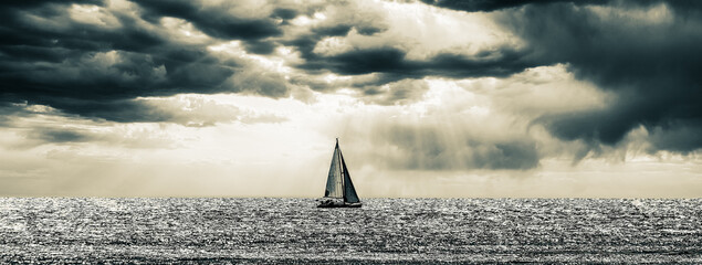 Black and white photo of a sailing boat on the sea in a dramatic sunset 