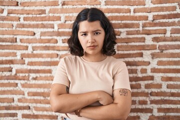 Young hispanic woman standing over bricks wall skeptic and nervous, disapproving expression on face with crossed arms. negative person.