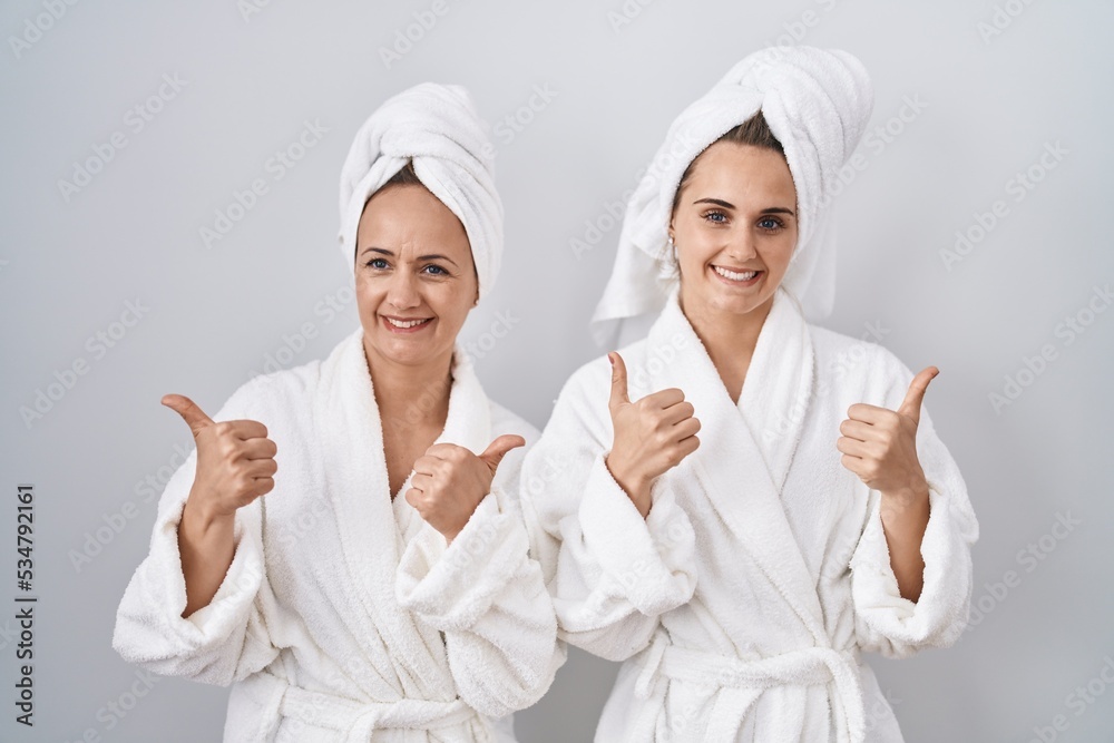 Canvas Prints Middle age woman and daughter wearing white bathrobe and towel success sign doing positive gesture with hand, thumbs up smiling and happy. cheerful expression and winner gesture.