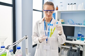 Young blonde woman wearing scientist uniform holding test tube at laboratory
