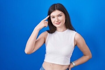 Fototapeta na wymiar Young caucasian woman standing over blue background smiling pointing to head with one finger, great idea or thought, good memory