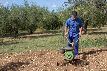 Image of a farmer who with a hand tiller prepares the land to cultivate his vegetable garden.
