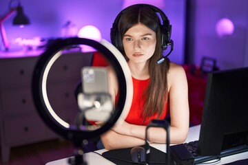 Young caucasian woman playing video games recording with smartphone thinking attitude and sober expression looking self confident