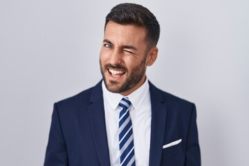 Handsome hispanic man wearing suit and tie winking looking at the camera with sexy expression,...