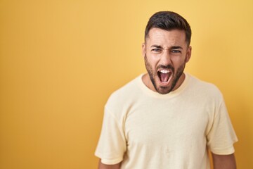 Obraz premium Handsome hispanic man standing over yellow background angry and mad screaming frustrated and furious, shouting with anger. rage and aggressive concept.
