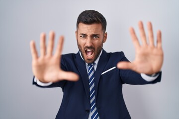 Handsome hispanic man wearing suit and tie doing stop gesture with hands palms, angry and...