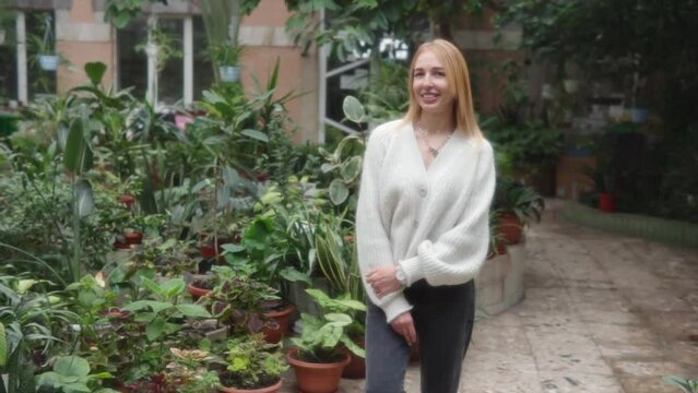 A young blonde girl poses in a white soft sweater in a greenhouse. 