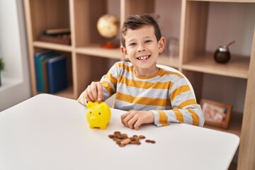 Blond child inserting coin on piggy bank at home
