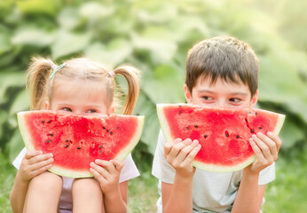 Two cheerful children eat slices of watermelon. Outdoors in summer park.