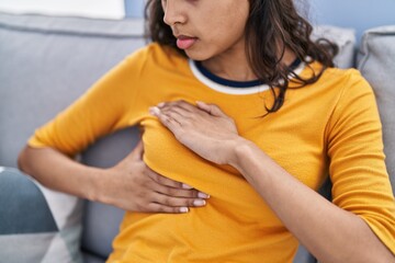 Young african american woman examining breast sitting on sofa at home