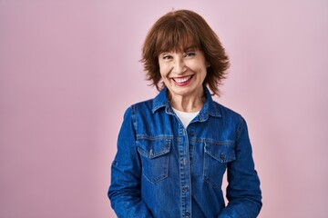 Middle age woman standing over pink background with hands together and crossed fingers smiling relaxed and cheerful. success and optimistic