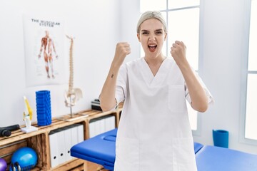 Obraz premium Young caucasian woman working at pain recovery clinic angry and mad raising fists frustrated and furious while shouting with anger. rage and aggressive concept.