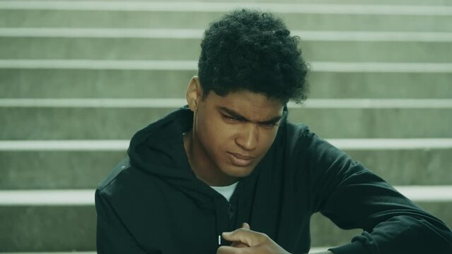 Furious teenager bumping fists while sitting on urban stairs alone, problems