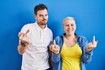 Young brazilian mother and son standing over blue background showing middle finger doing fuck you bad expression, provocation and rude attitude. screaming excited