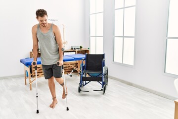 Fototapeta na wymiar Young hispanic man smiling confident walking using crutches at clinic