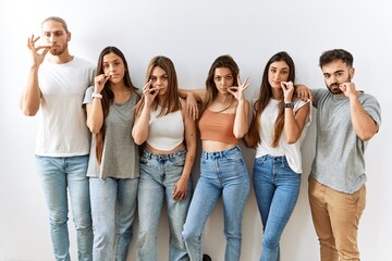 Group of young friends standing together over isolated background mouth and lips shut as zip with...