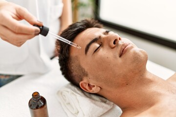 Obraz na płótnie Canvas Young hispanic man relaxed having facial treatment at beauty center