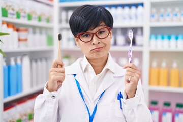 Young asian woman with short hair doing toothbrush comparative at pharmacy skeptic and nervous, frowning upset because of problem. negative person.