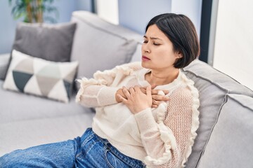 Young chinese woman sitting on sofa with hands on heart at home