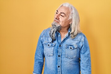 Middle age man with grey hair standing over yellow background looking away to side with smile on face, natural expression. laughing confident.