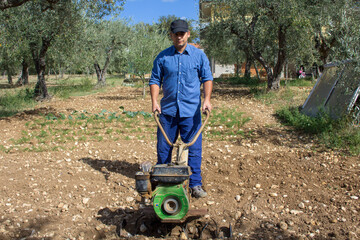 Farmer with a tiller while he tills a land for the cultivation of the vegetable garden. Fertile...