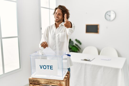 Young hispanic man voting putting envelop in ballot box pointing fingers to camera with happy and funny face. good energy and vibes.