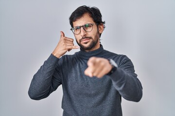 Handsome latin man standing over isolated background smiling doing talking on the telephone gesture...