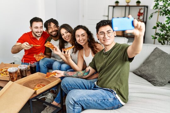 Group of young friends smiling happy eating italian pizza make selfie by the smartphone at home.