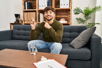 Obraz premium Arab man with beard working on depression at therapy office smiling and looking at the camera pointing with two hands and fingers to the side.