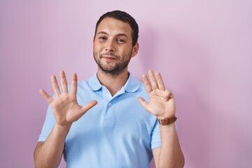 Hispanic man standing over pink background showing and pointing up with fingers number nine while...