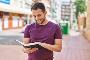 Young man smiling confident reading book at street