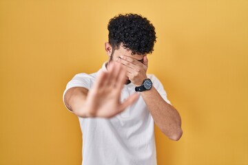 Arab man standing over yellow background covering eyes with hands and doing stop gesture with sad and fear expression. embarrassed and negative concept.