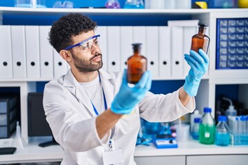 Young arab man wearing scientist uniform holding bottles at laboratory
