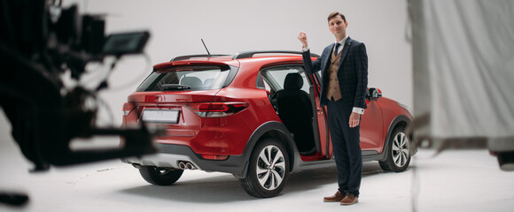 Naklejka premium Professional male actor works in the frame on the set. Shooting with a car on a large white cyclorama.