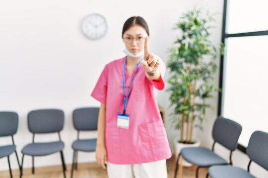 Young Asian Nurse Woman At Medical Waiting Room Pointing With Finger Up And Angry Expression, Showing No Gesture