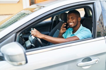 Young african american man talking on the smartphone sitting on car at street