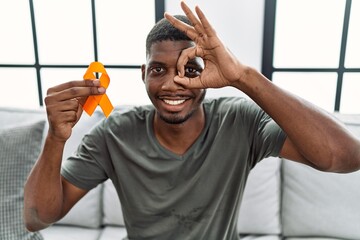 Young african american man holding awareness orange ribbon sitting on the sofa smiling happy doing...