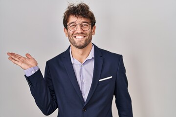 Hispanic business man wearing glasses smiling cheerful presenting and pointing with palm of hand looking at the camera.